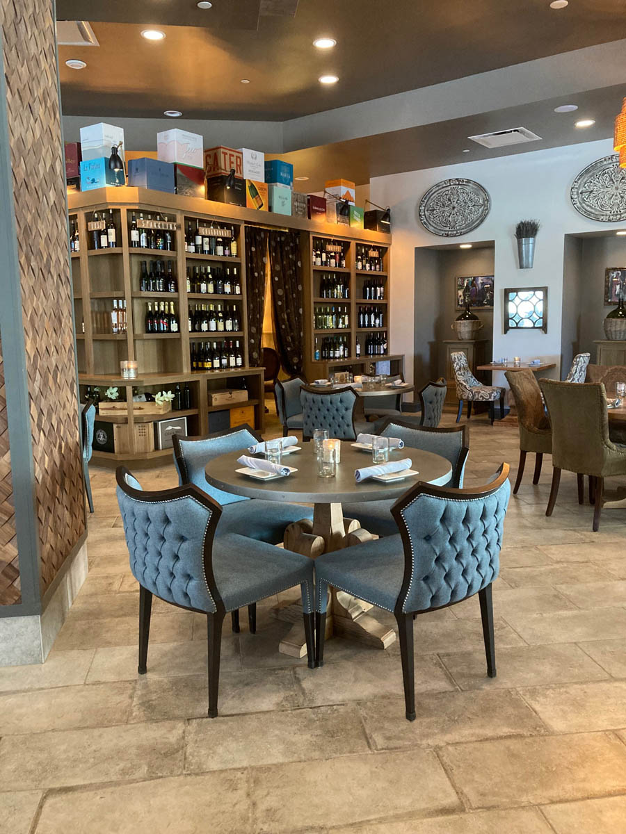 Round tables for four with tufted blue seating near wall of wines in shelving at Napa Kitchen + Bar in downtown Toledo, Ohio.