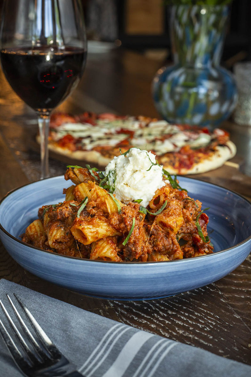 Plated Rigatoni Rustica with glass of red wine and pizza served at Napa Kitchen & Bar in Columbus, Ohio.