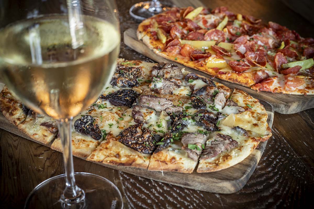 Glass of white wine in foreground with two pizzas behind at Napa Kitchen & Bar