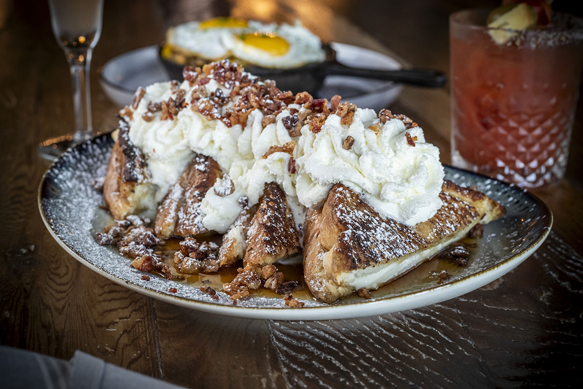 Stuffed French Toast with swirls of whipped cream and pecans on table with brunch cocktails at Napa Kitchen & Bar