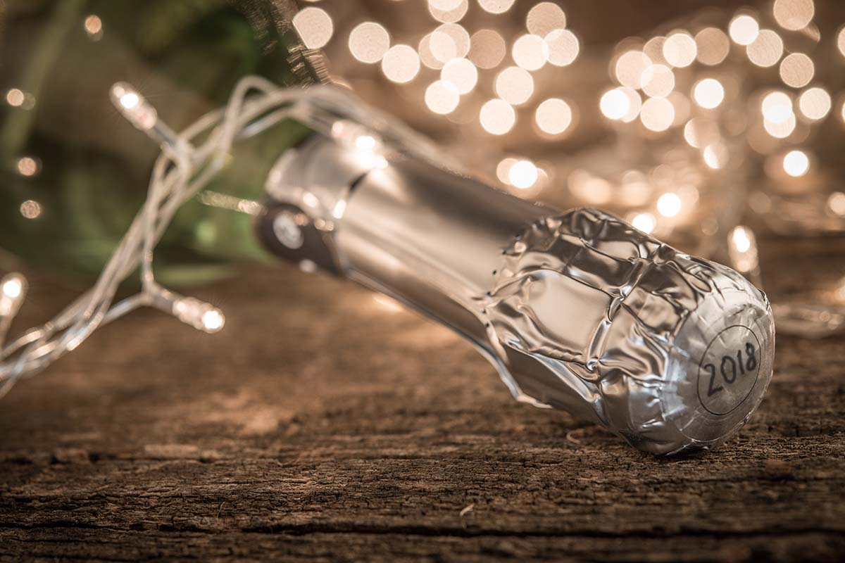 Unopened bottle of champagne on its side with decorate white light strand around it.